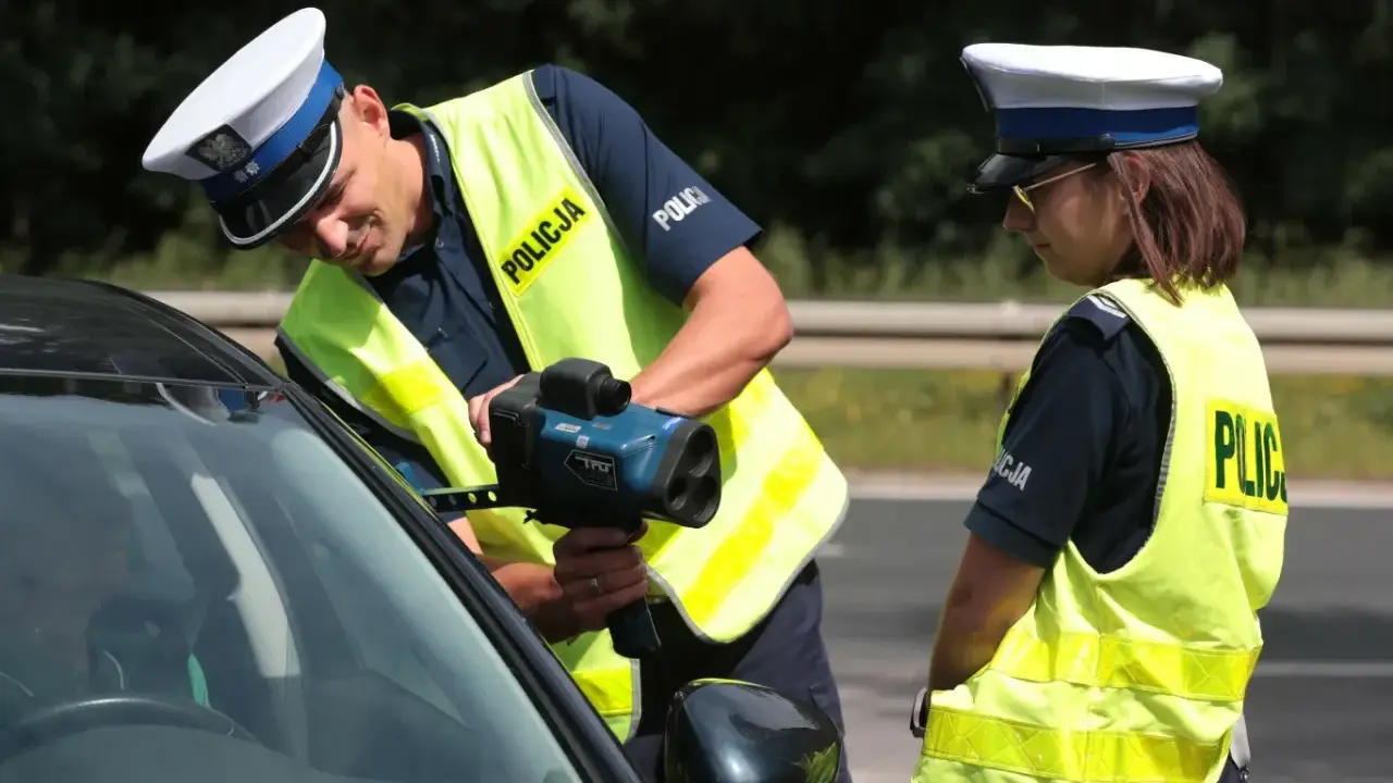 Policjanci w kamizelkach odblaskowych mierzą prędkość samochodu radarem.