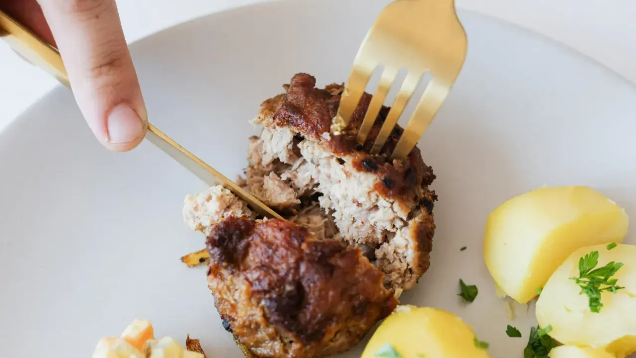 Kotlety mielone przepis babci: soczysty kotlet rozkrajany widelcem, obok ziemniaczki i surówka.