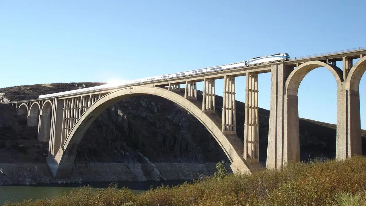 Un tren de alta velocidad cruza un imponente puente arco de hormigón sobre un embalse.