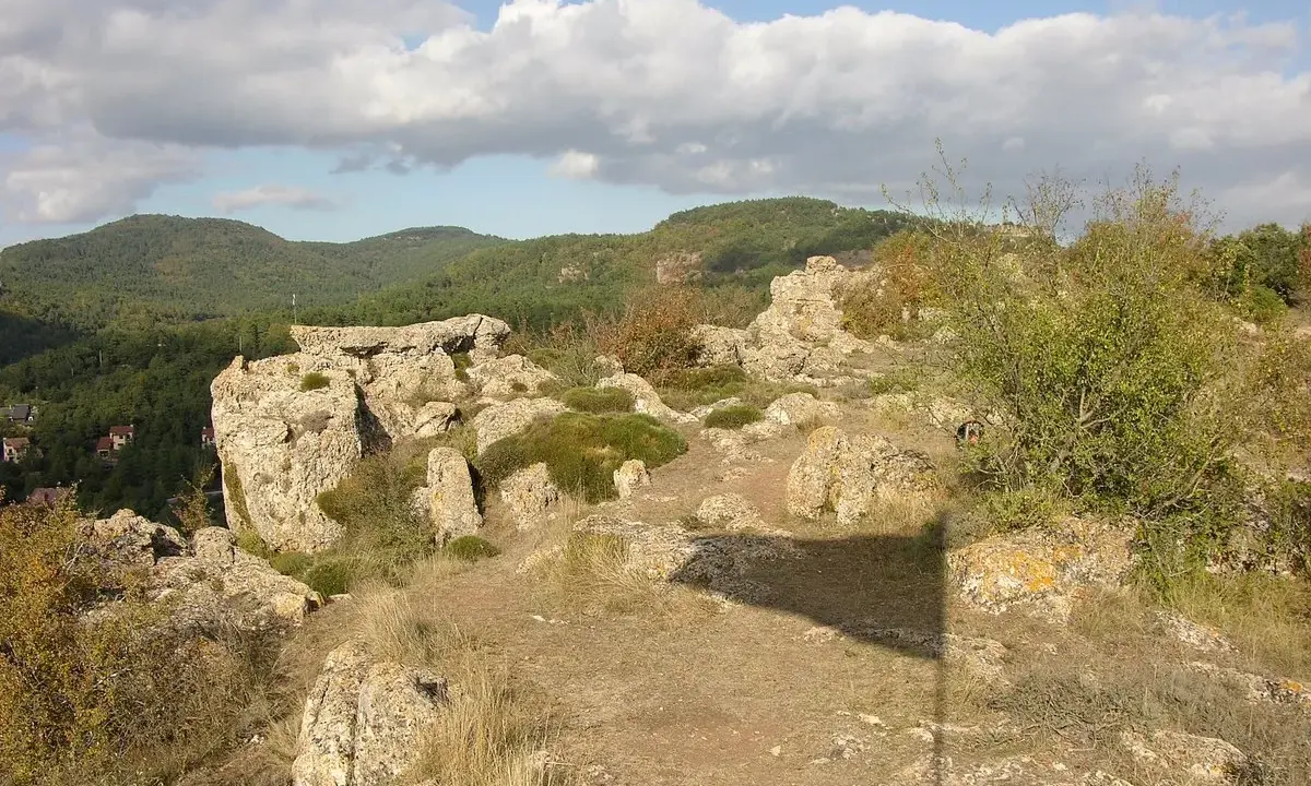 Paisaje rocoso con vegetación y colinas boscosas al fondo. Un lugar ideal que ver en Prades para disfrutar de la naturaleza.