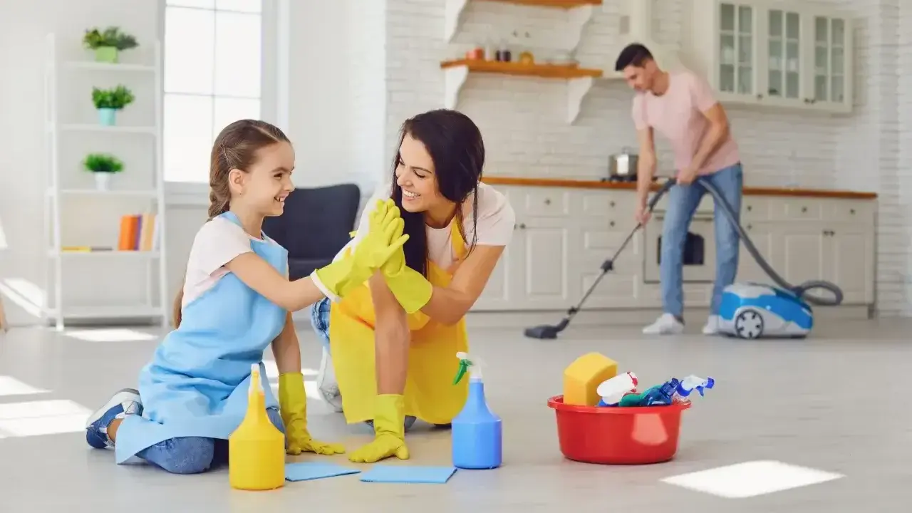 Mama i córka świętują udane porządki. W tle tata odkurza. To świetny przykład, jak obowiązki 9 latka w domu mogą być wspólną zabawą.
