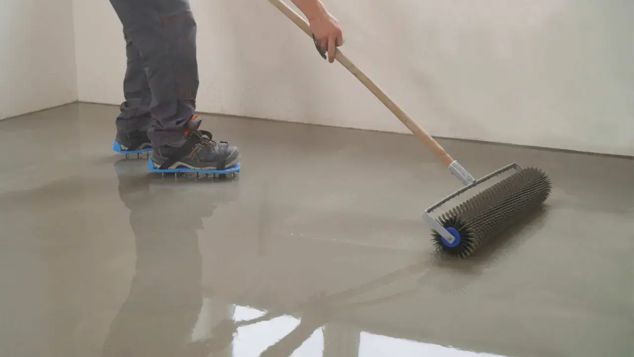 Persona con calzado de púas usando un rodillo para nivelar un suelo recién vertido.