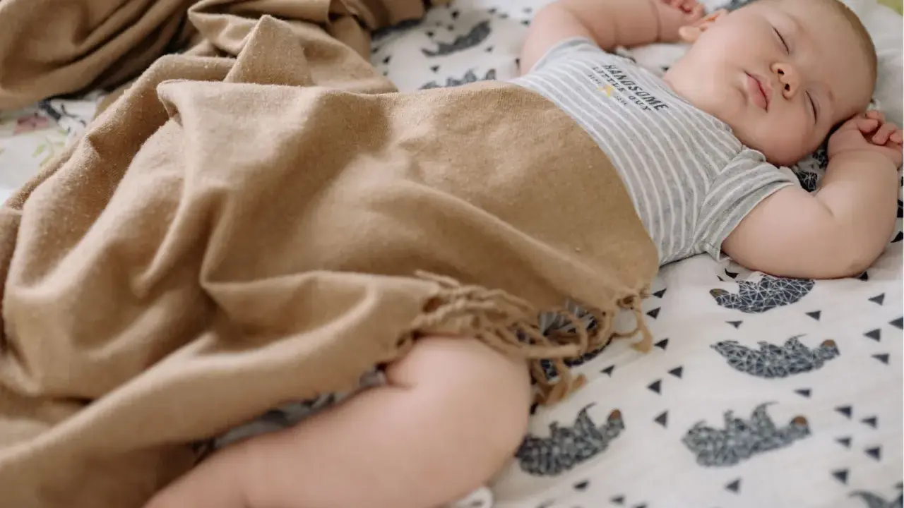 Bebé durmiendo plácidamente, envuelto en una manta de tonos tierra. Las medidas del arrullo bebé son ideales para su comodidad.