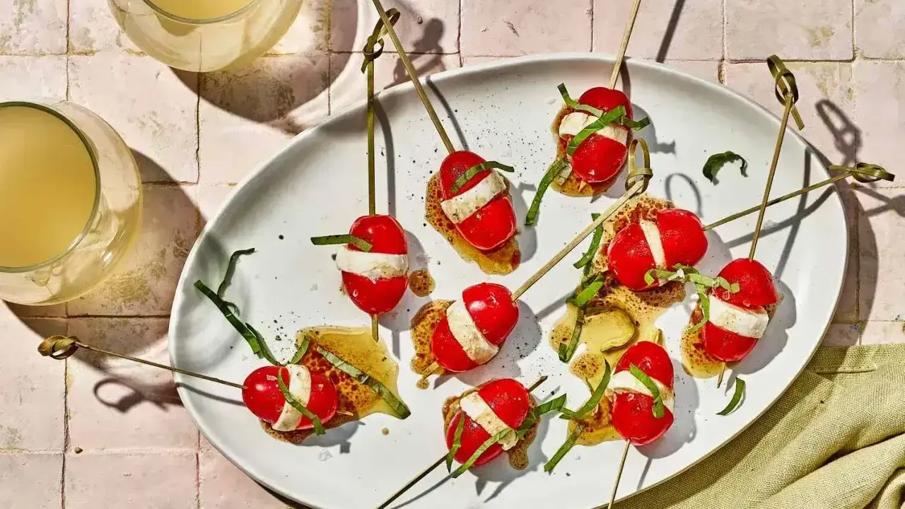 Szybkie przekąski na ognisko: pomidorki koktajlowe z mozzarellą i bazylią na patyczkach, polane sosem.