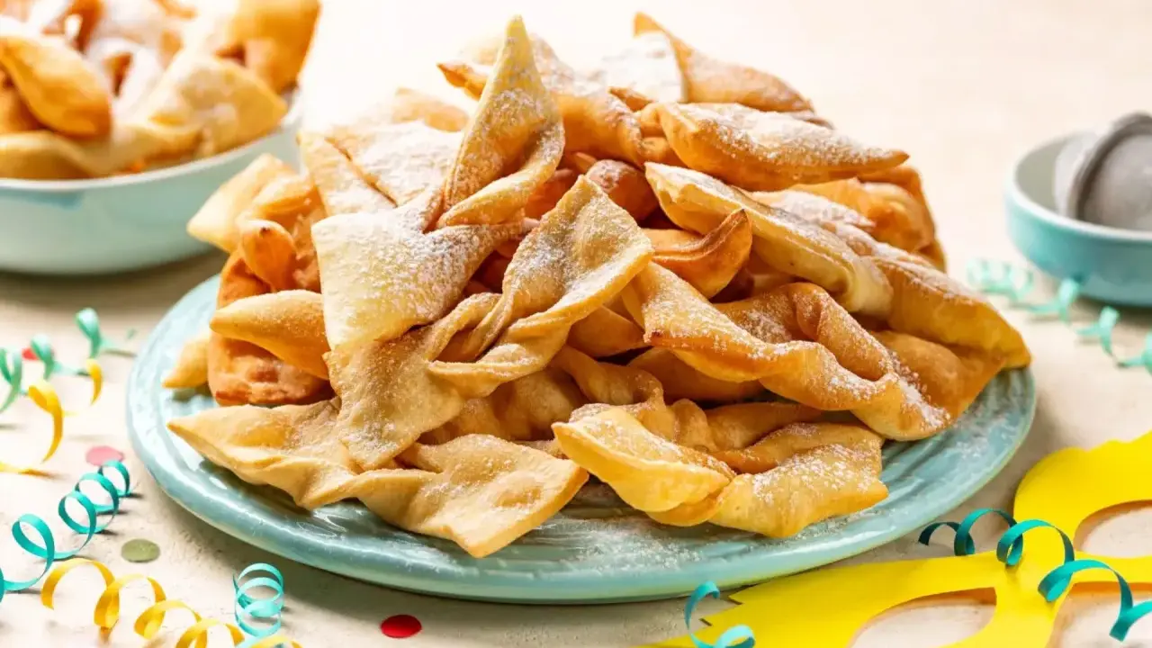 Un piatto colmo di chiacchiere, dolci tipici di Carnevale, cosparse di zucchero a velo. Festa e gusto, ecco cosa si mangia a Carnevale!