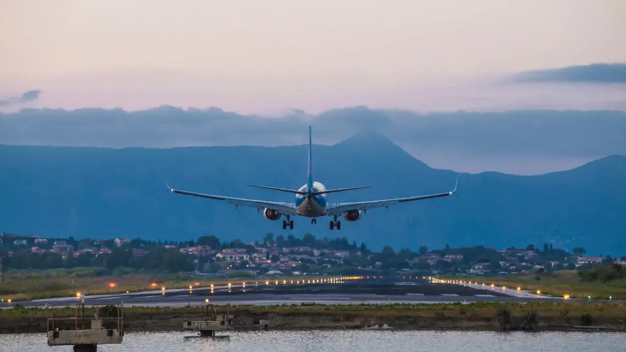 Ett flygplan landar vid Korfu flygplats i skymningen. Landningsbanans ljus lyser upp vägen.