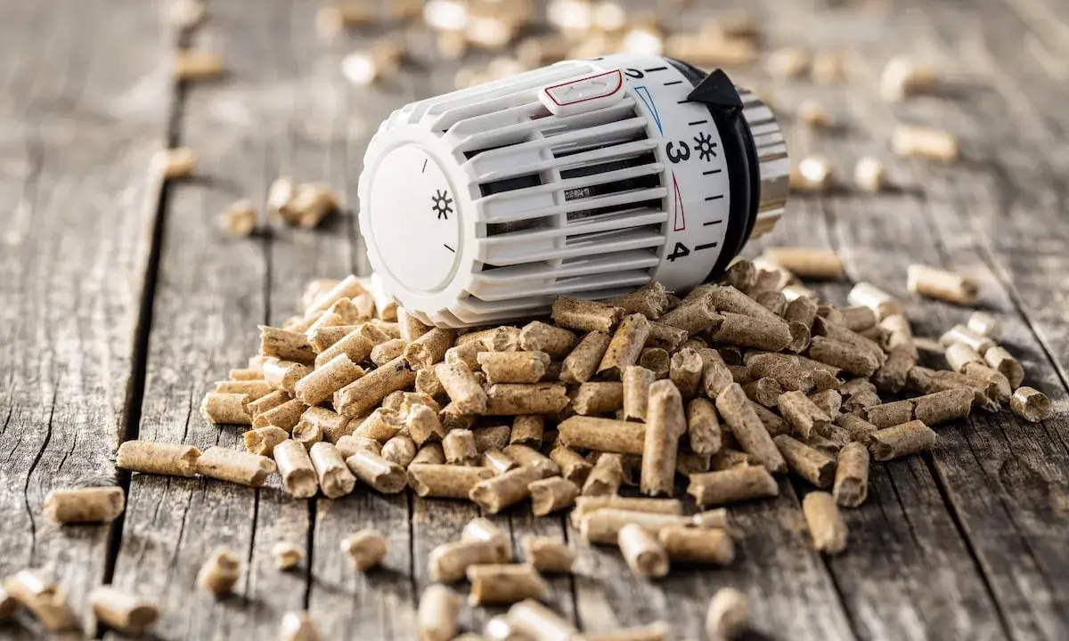 Ein Thermostat auf einem Haufen Holzpellets. Die Frage "wie lange heizt man mit 1 tonne pellets" wird hier visuell thematisiert.