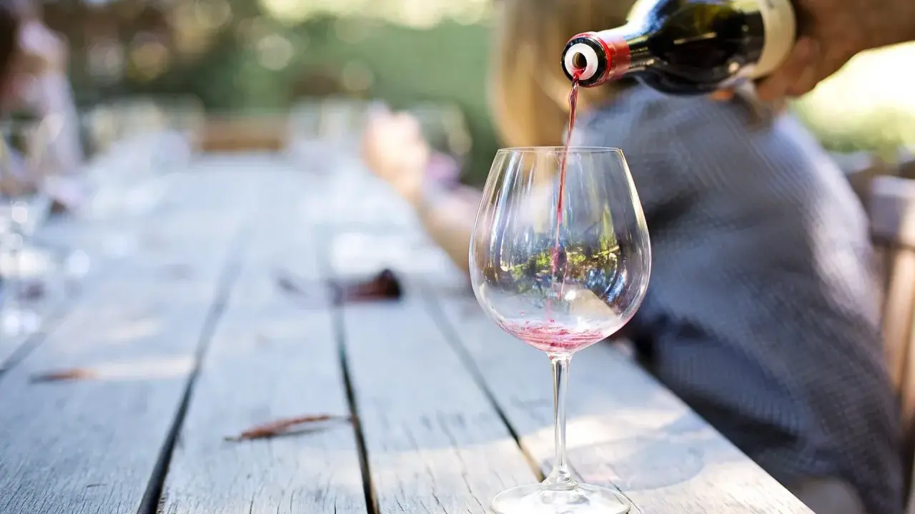 Czerwone wino nalewane z butelki do kieliszka na drewnianym stole.