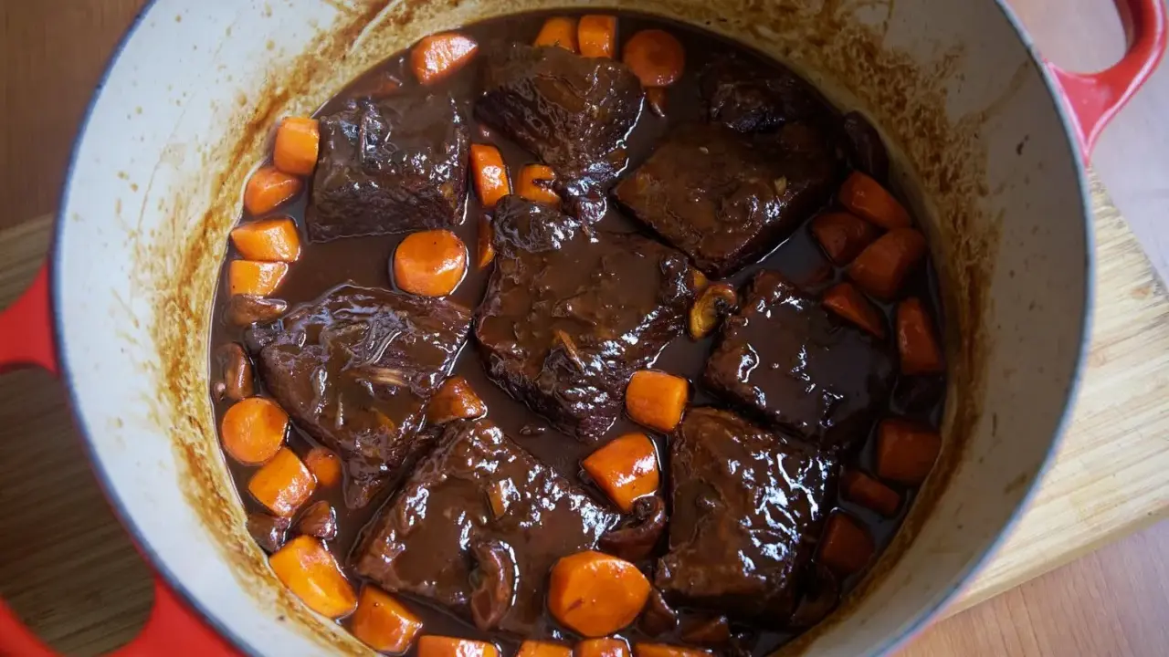 Boeuf bourguignon casero en olla roja, con trozos de carne tierna, zanahorias y champiñones en una rica salsa.