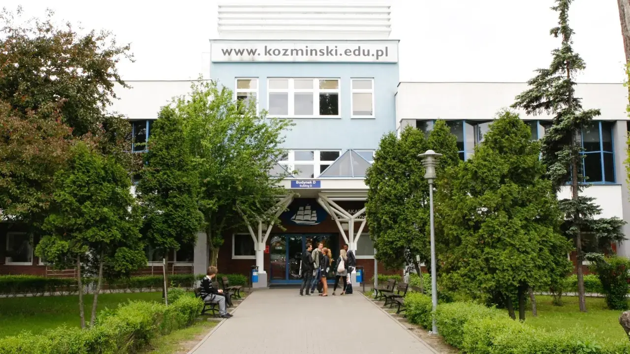 Studenci przed budynkiem koźmin uczelnia. W tle logo uczelni i napis www.kozminiński.edu.pl.