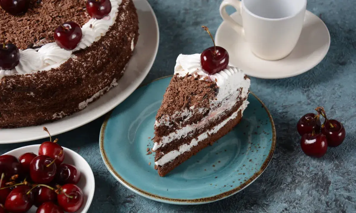 Una porción de tarta Selva Negra, con capas de bizcocho de chocolate, nata y cerezas, decorada con virutas de chocolate y una cereza encima.
