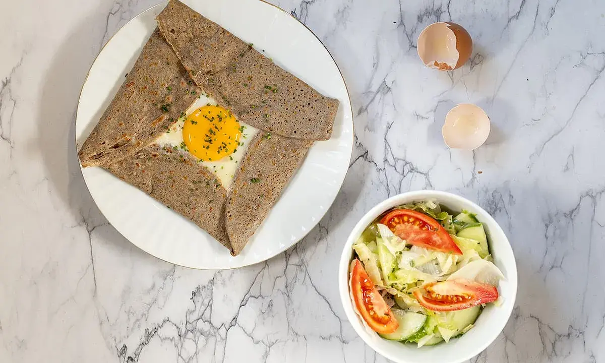 Une délicieuse crêpe complète bretonne avec un œuf coulant, accompagnée d'une salade fraîche.