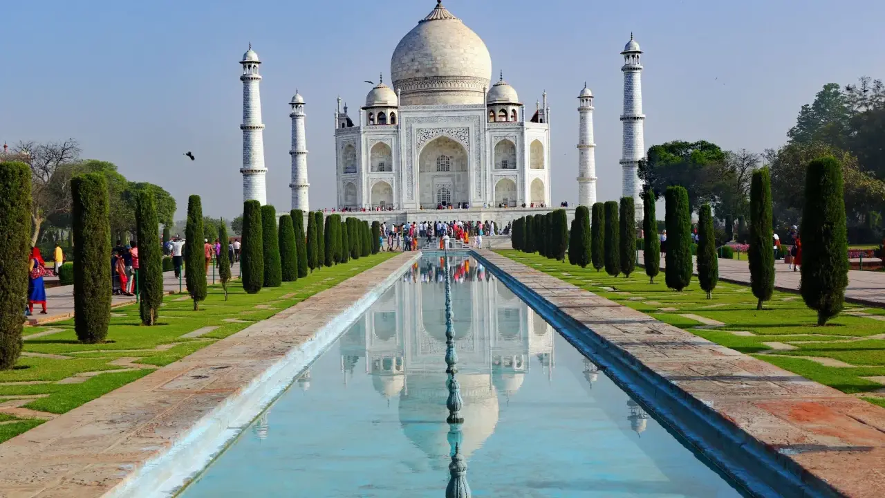 Majestatyczny Taj Mahal w Indiach odbija się w spokojnej wodzie, otoczony zielonymi ogrodami i strzelistymi cyprysami.