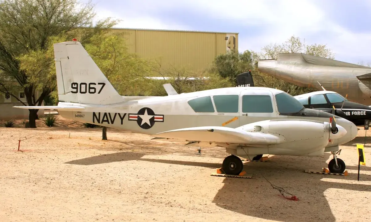 Ein zweimotoriges Piper-Flugzeug der US Navy mit der Kennung 9067 steht auf einem staubigen Flugplatz.
