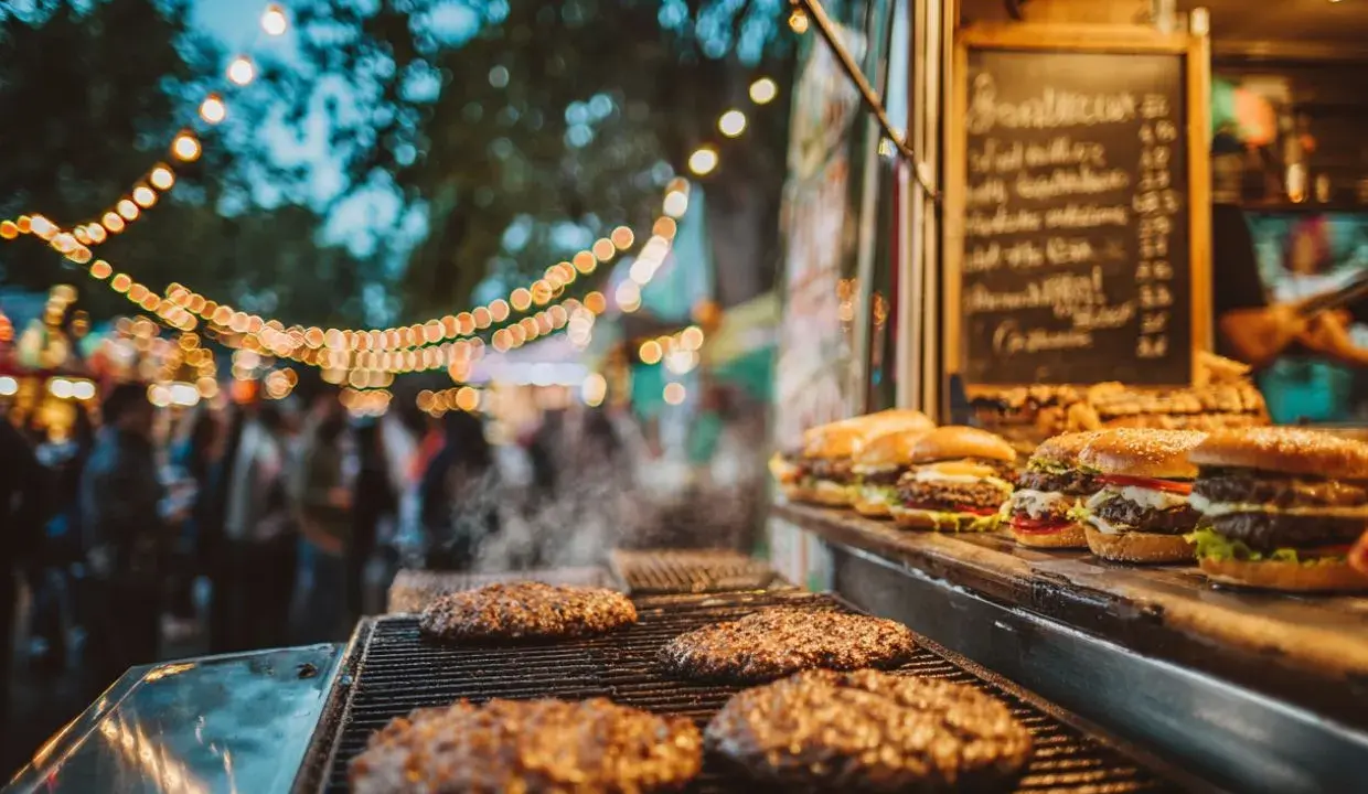 Hamburguesas humeantes en parrilla, listas para servir en un food truck. Un ejemplo de cómo montar un food truck exitoso con ambiente festivo.