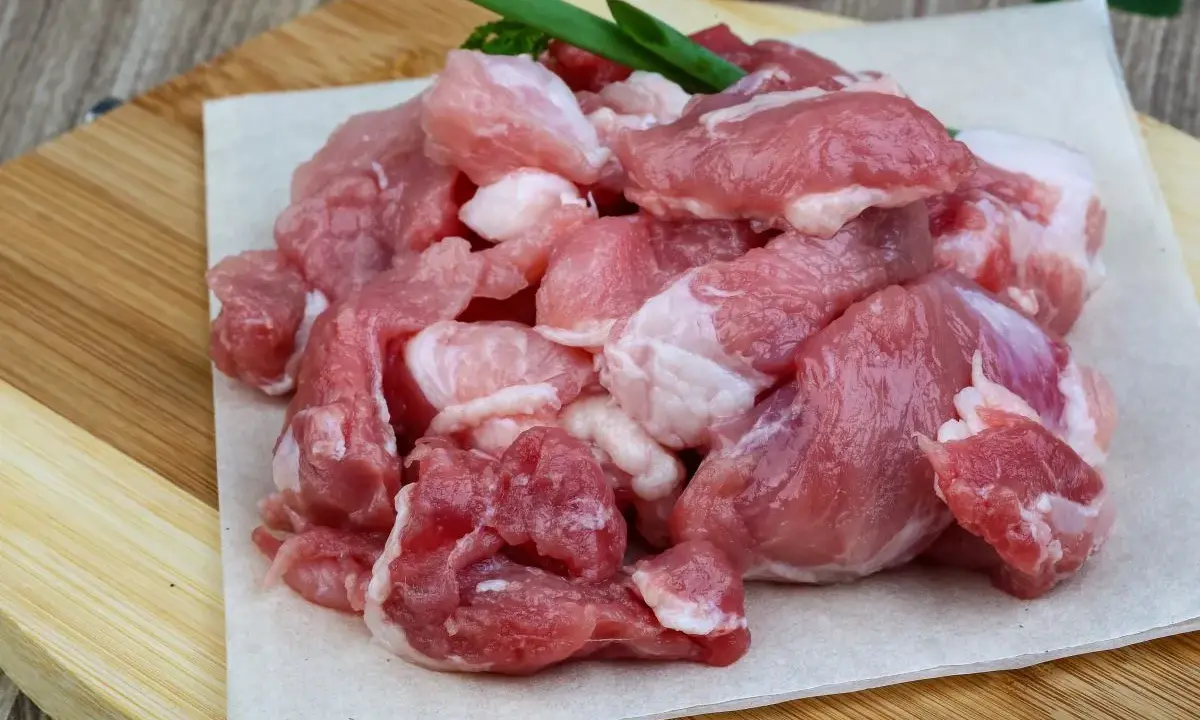 Surowe, pokrojone w kostkę mięso wieprzowe, idealne na gulasz. W tle czosnek i papryczki chili.