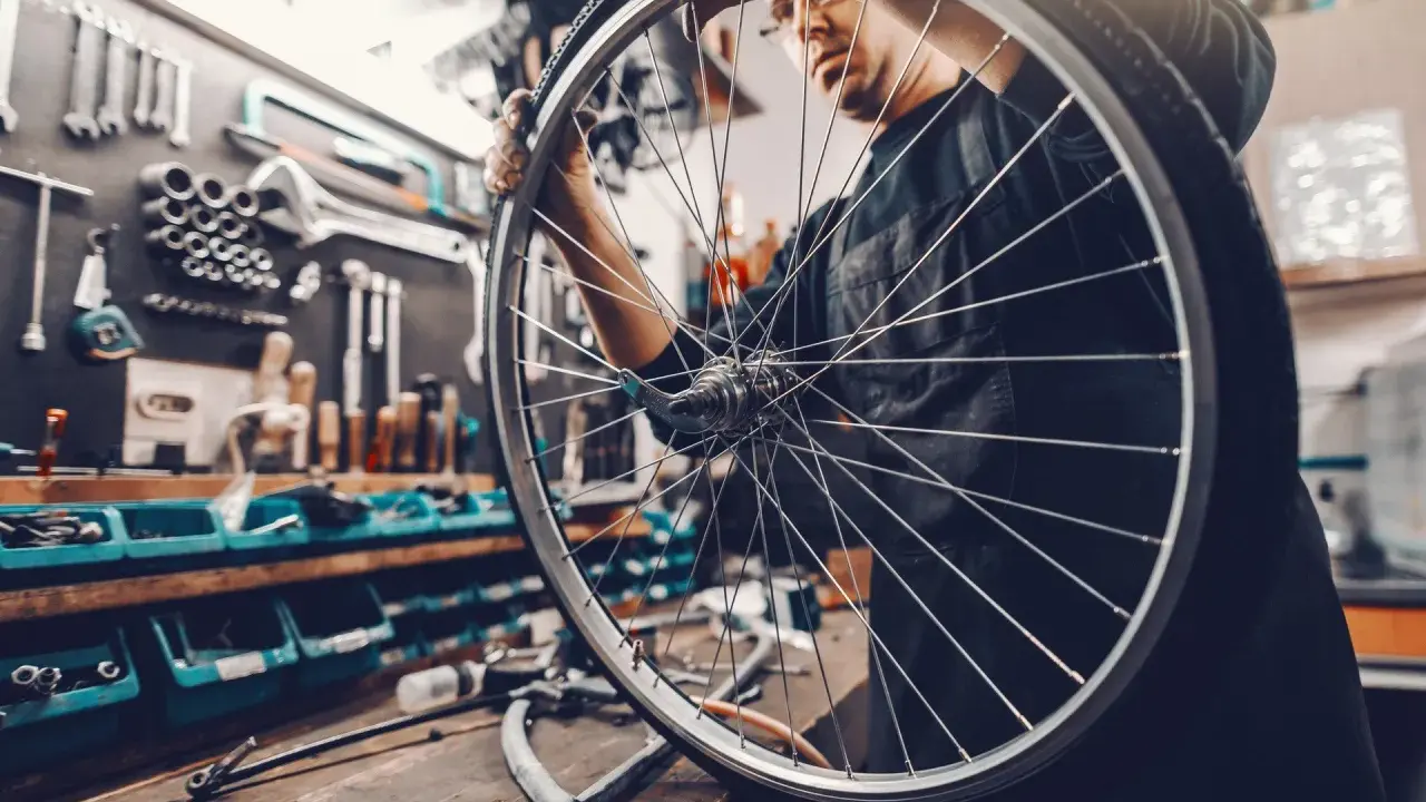 Mechanik sprawdza układy w rowerze, trzymając koło. W tle warsztat z narzędziami.