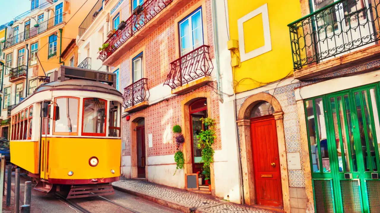 Gelber Straßenbahn fährt durch eine enge Gasse mit bunten Häusern. Ein typisches Bild der Umweltzone Lissabon.