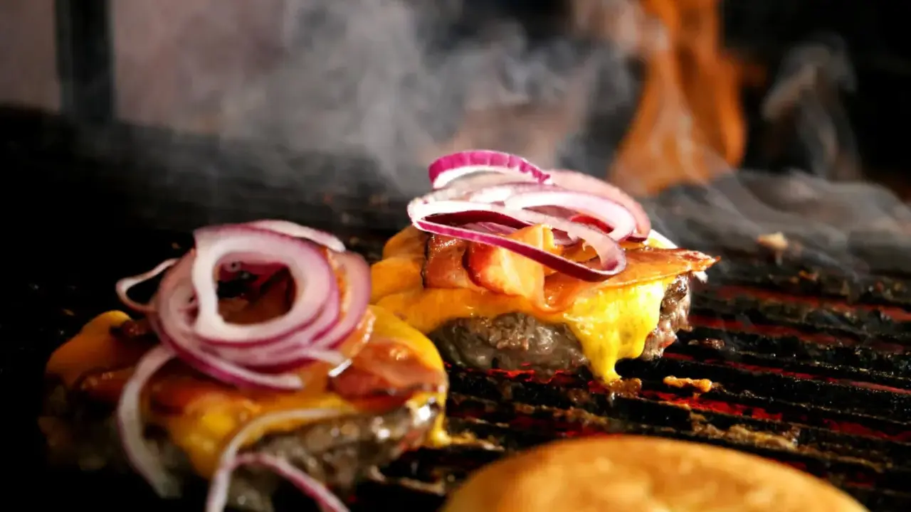 Pyszne burgery z grilla, z rozpływającym się serem i chrupiącym boczkiem, unoszą się w dymie.