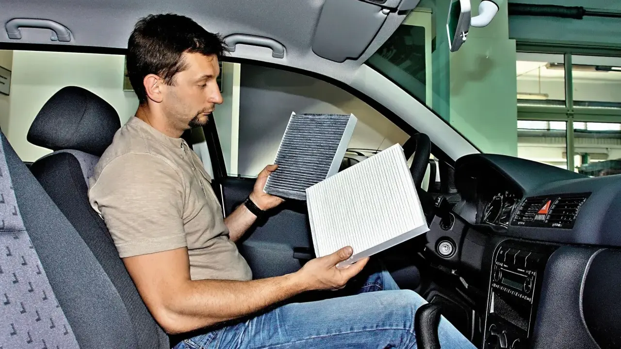 Mężczyzna w kabinie Renault Megane 3 porównuje stary i nowy filtr kabinowy, przygotowując się do jego wymiany.