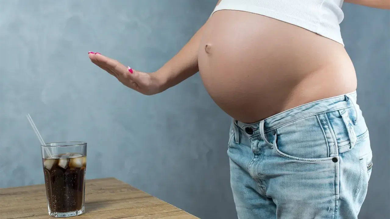 Schwanger und verzichtet auf Cola. Eine Hand weist ein Glas Cola mit Eis und Strohhalm ab.