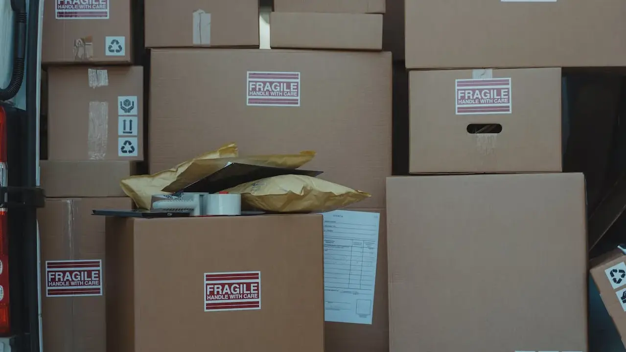 Stos kartonów, w tym oznaczone jako "FRAGILE", gotowych do wysyłki. Czy do reklamacji potrzebny jest karton? Zazwyczaj tak, aby zabezpieczyć towar.