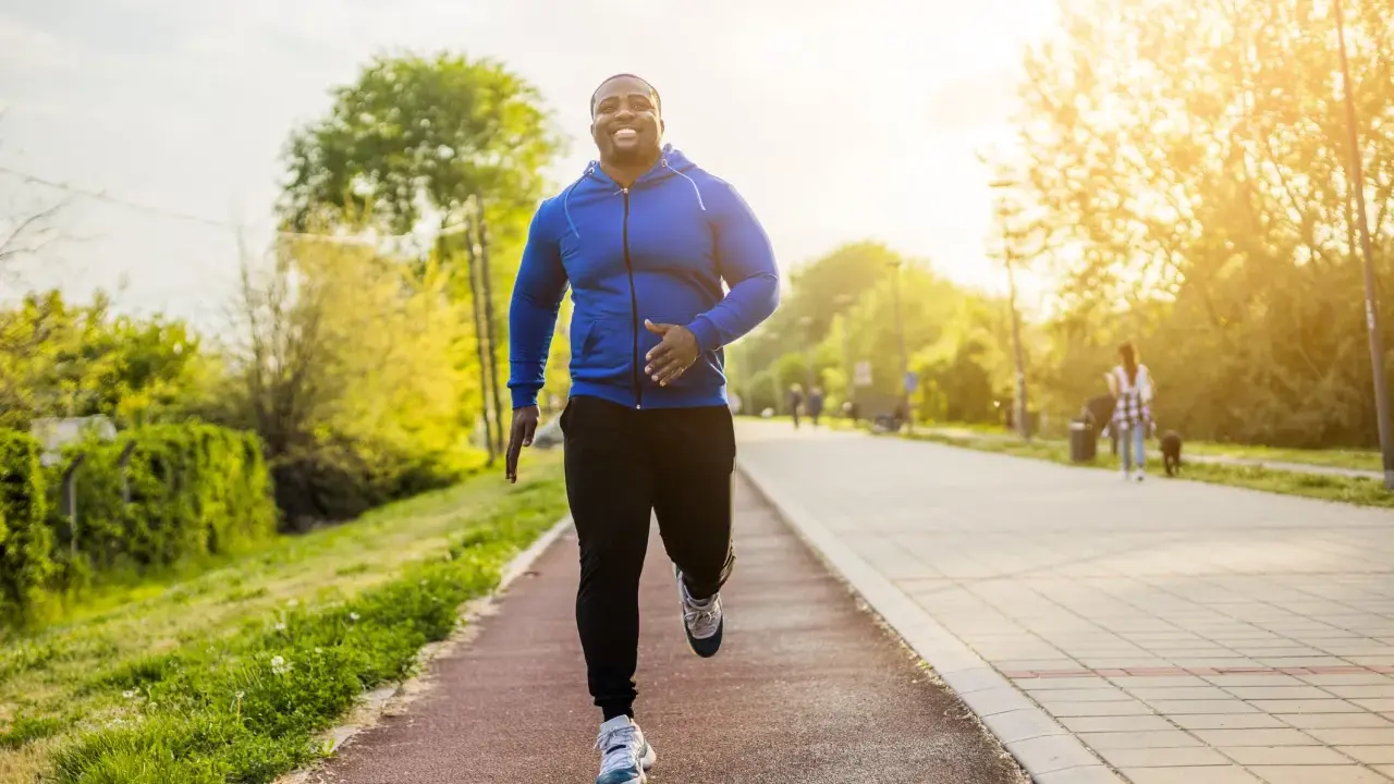 Glücklicher Mann beim Laufen im Park. Sein Training laufen im Sonnenschein macht ihn fit und gesund.