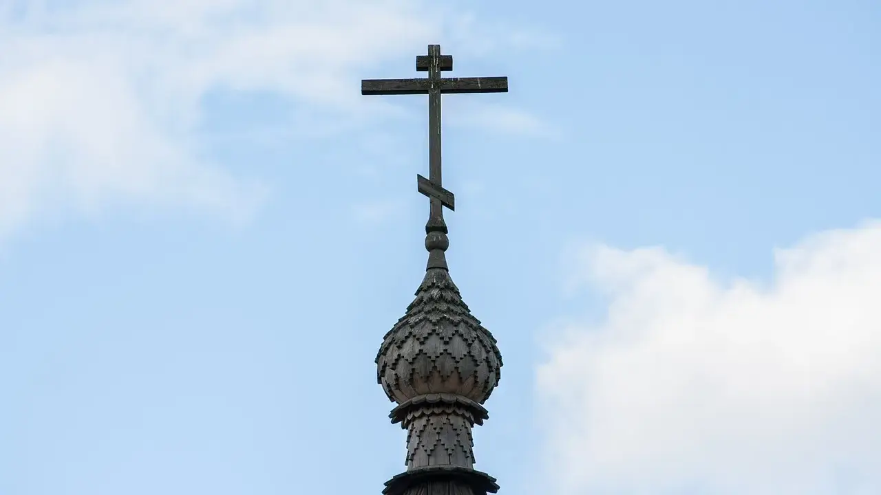 Drewniany krzyż na kopule cerkwi, symbol religii w Gruzji, na tle błękitnego nieba z chmurami.