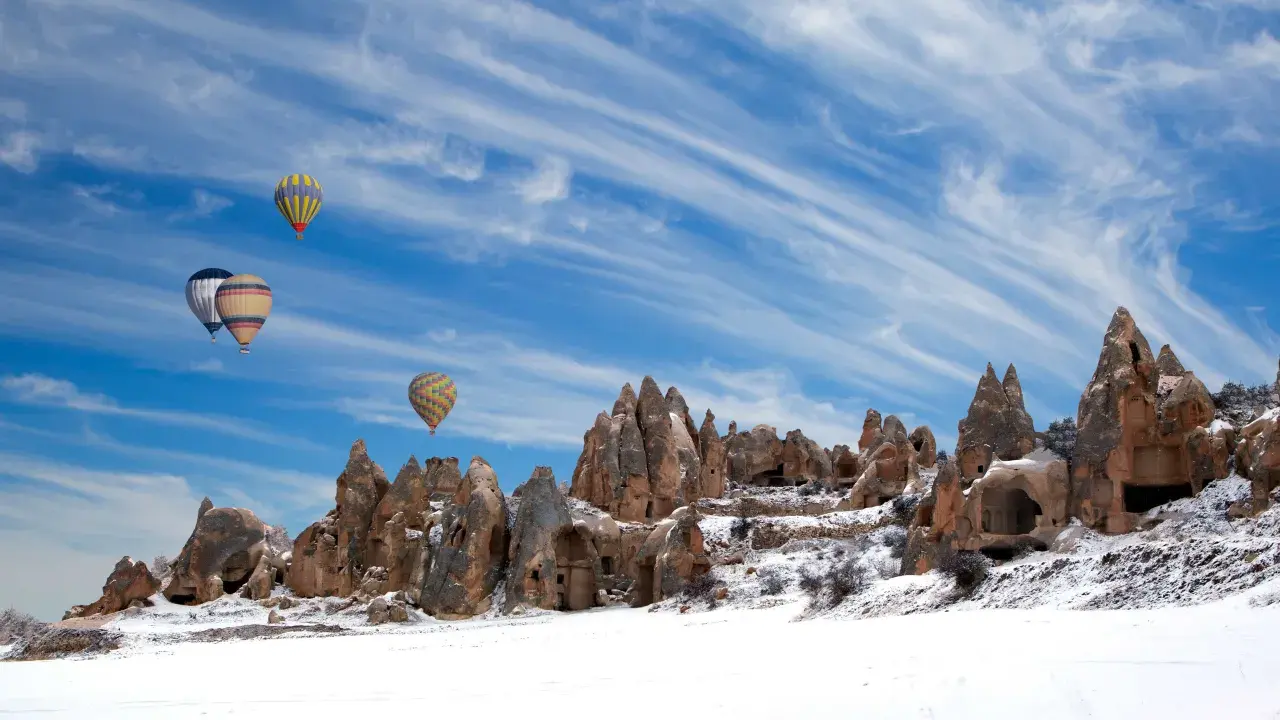 Balony unoszą się nad ośnieżonymi formacjami skalnymi w Kapadocji. Czy w Turcji pada śnieg? Tak, zimą krajobraz potrafi być bajkowy.