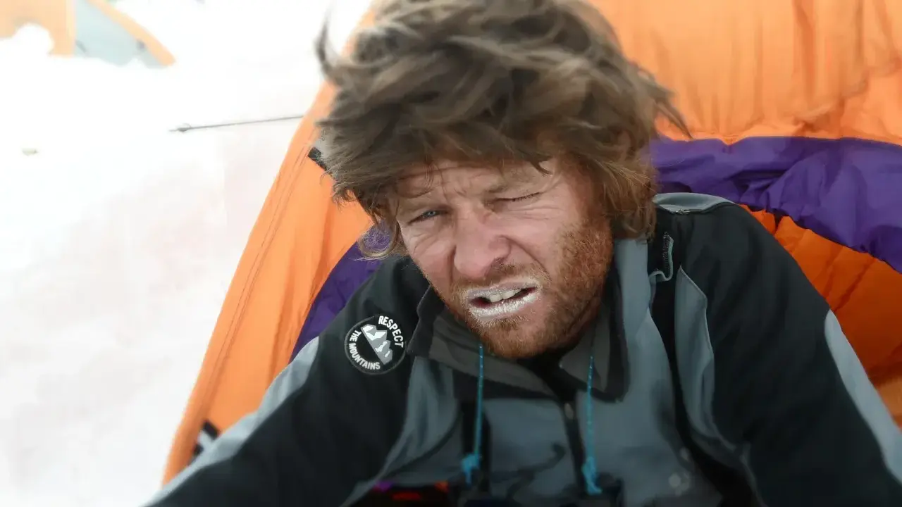 Zmęczony alpinista z białym proszkiem na ustach, być może lek na chorobę wysokościową, w namiocie na śniegu.