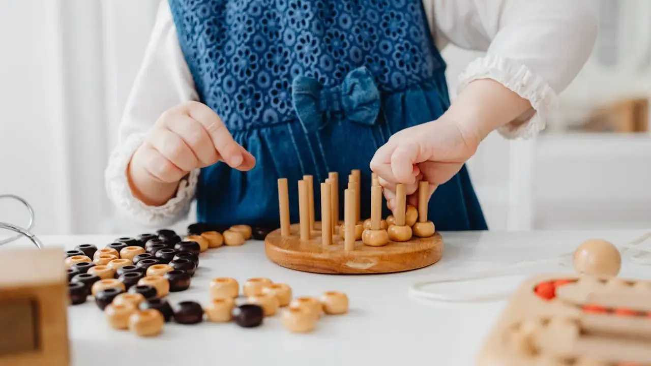 Niña con vestido azul jugando con cuentas de madera y un juego de encaje, parte de juegos para superar el mutismo selectivo.