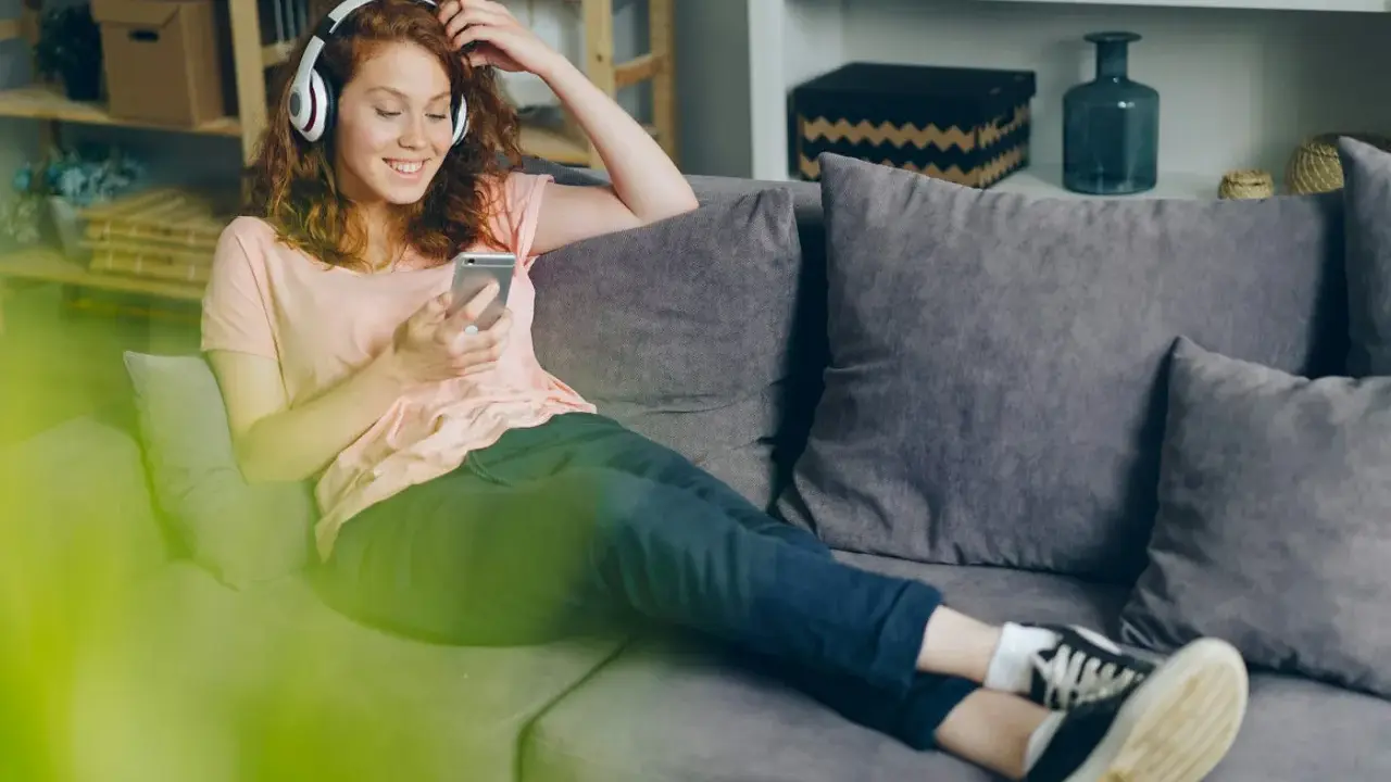 Dziewczyna z rudymi włosami słucha muzyki Indili, przeglądając telefon na kanapie. Jej uśmiech sugeruje, że to jej ulubiona love story.