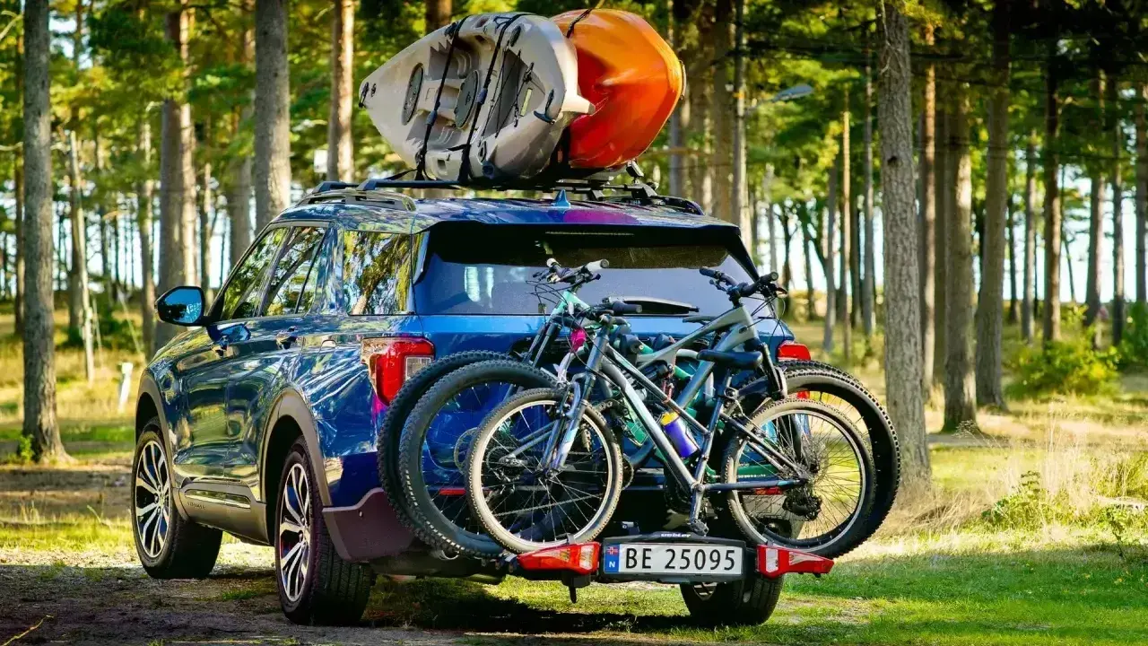 Niebieski SUV z dwoma rowerami na bagażniku i kajakami na dachu samochodu, gotowy na przygodę w lesie.