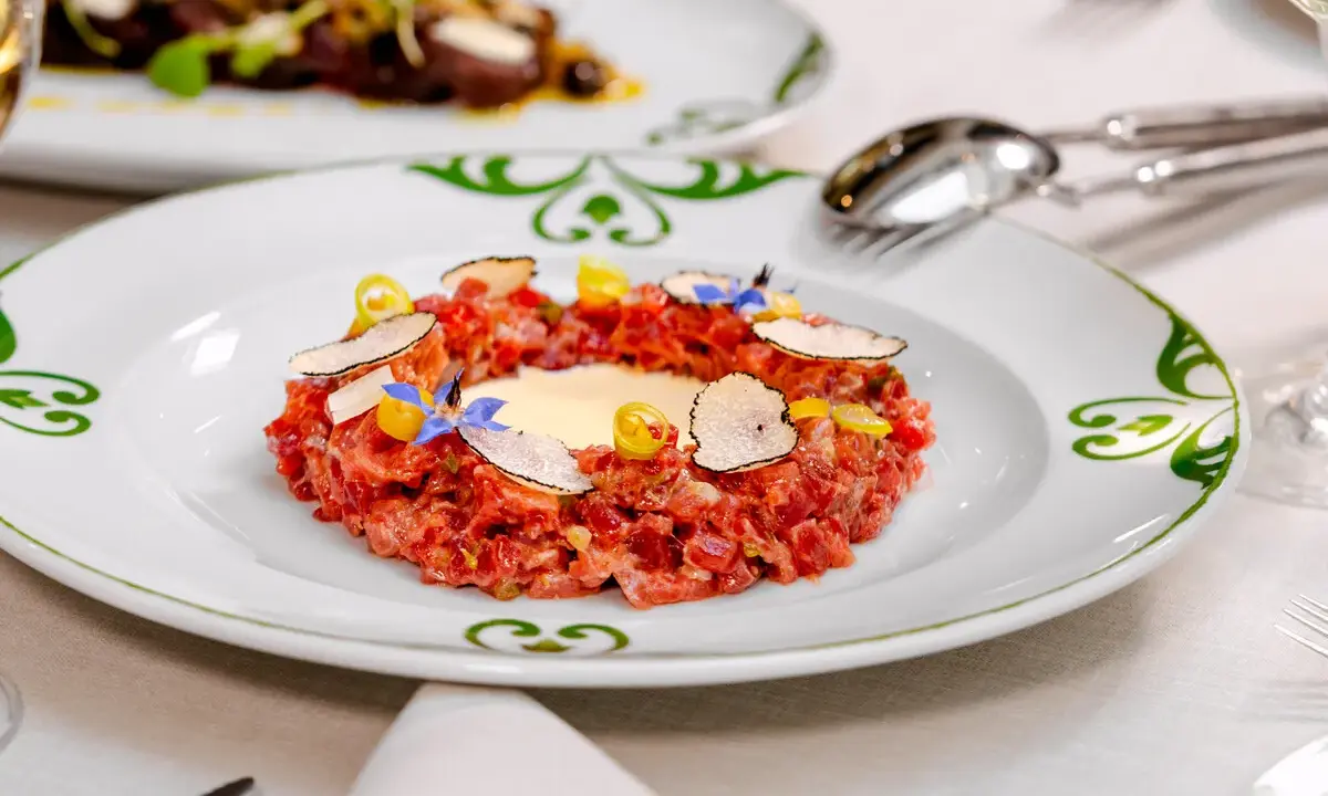 Delicioso tartar de atún fresco, adornado con láminas de trufa negra, flores comestibles y un toque de amarillo vibrante.