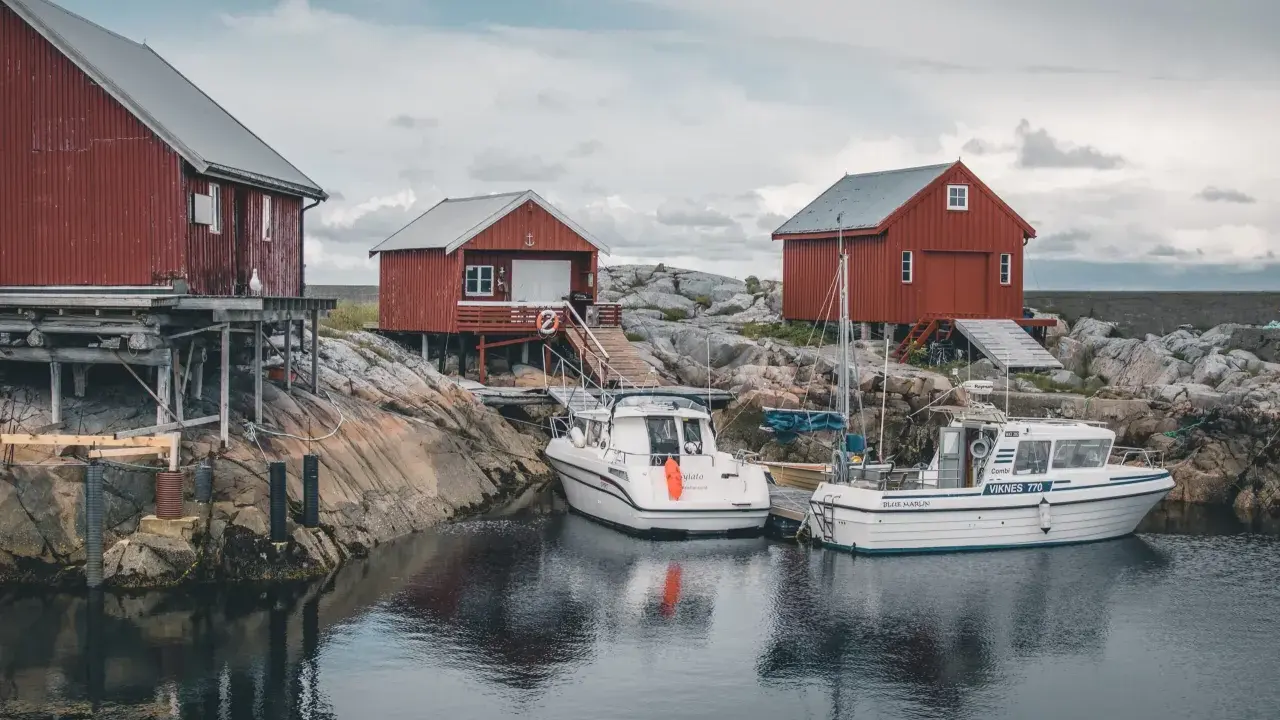 Norwegia: praca w norwegii dla par z zakwaterowaniem. Czerwone domki rybackie i łodzie przy skalistym brzegu.