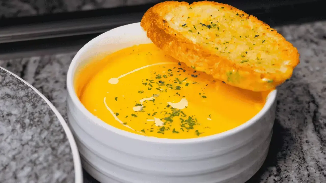 Bol de soupe orange crémeuse garni d'herbes et d'une tranche de pain à l'ail.