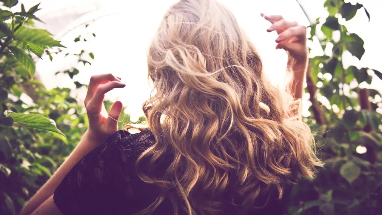 Frau mit welligem Haar, das einen subtilen Reverse Balayage-Effekt zeigt. Vorher-Nachher-Verwandlung für einen natürlichen Look.