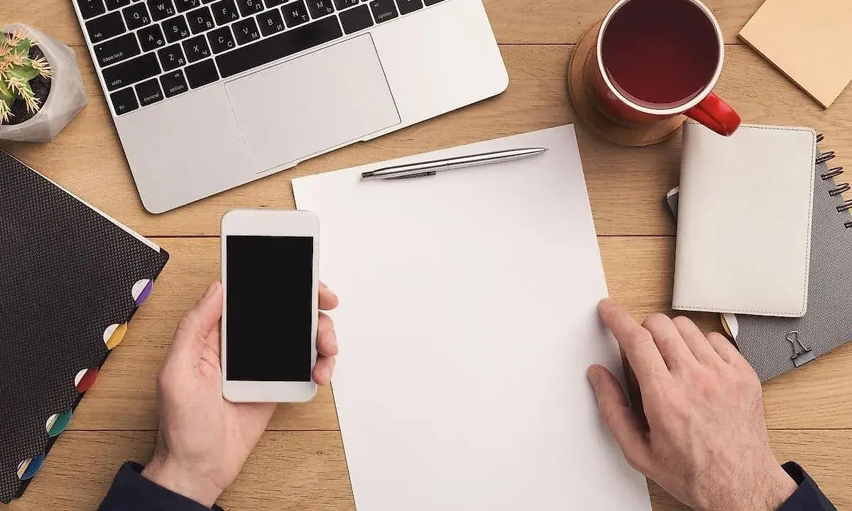 Przygotowuję formalny list. Na biurku leży laptop, telefon, kubek z herbatą i notatnik.