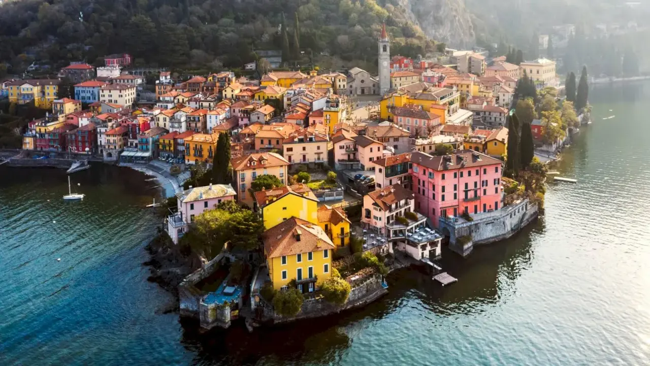Färgstark by vid en sjö i norra Italien, med hus i gult, rosa och orange som klättrar uppför en sluttning.