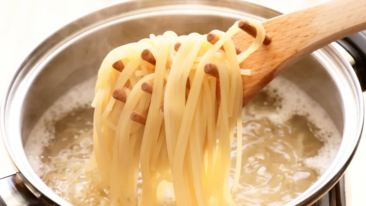 Une louche en bois retire des spaghettis bouillis à la perfection, juste al dente, d'une casserole d'eau bouillante.