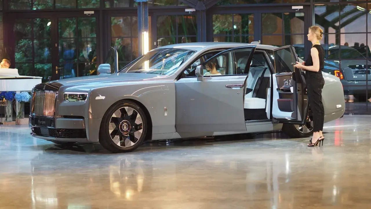 Elegancki szary Rolls-Royce Phantom z otwartymi drzwiami, obok którego stoi kobieta. Poznaj jego wyjątkową rolls royce phantom cena.