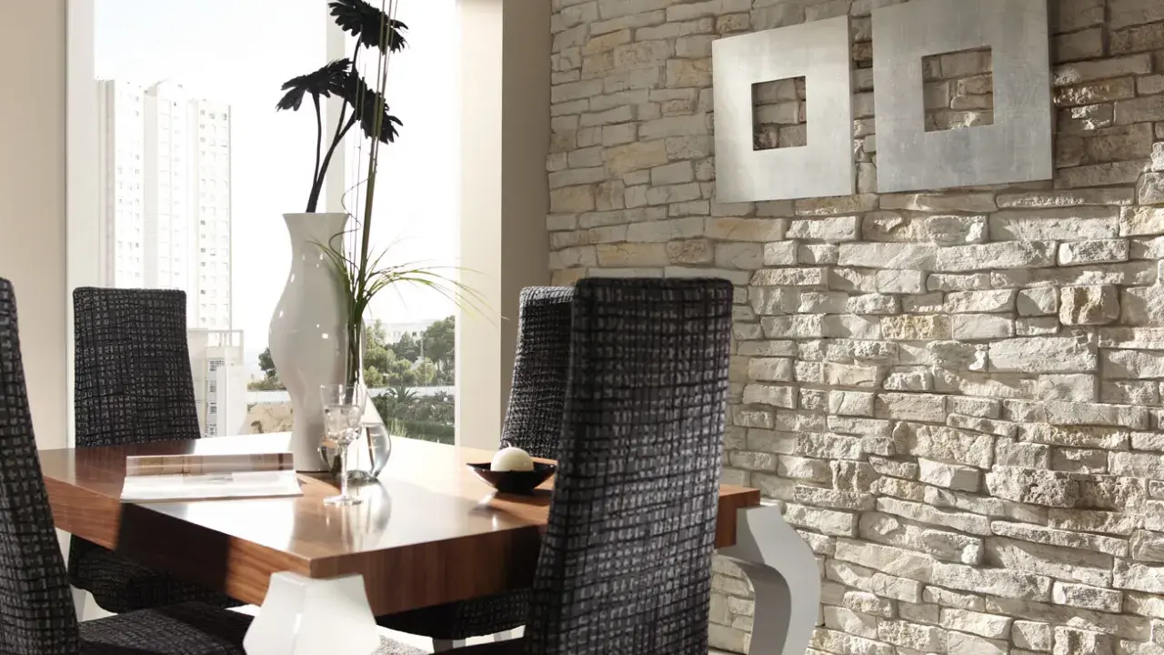 Comedor moderno con mesa de madera, sillas tapizadas y una pared con distintos tipos de revestimientos de piedra.