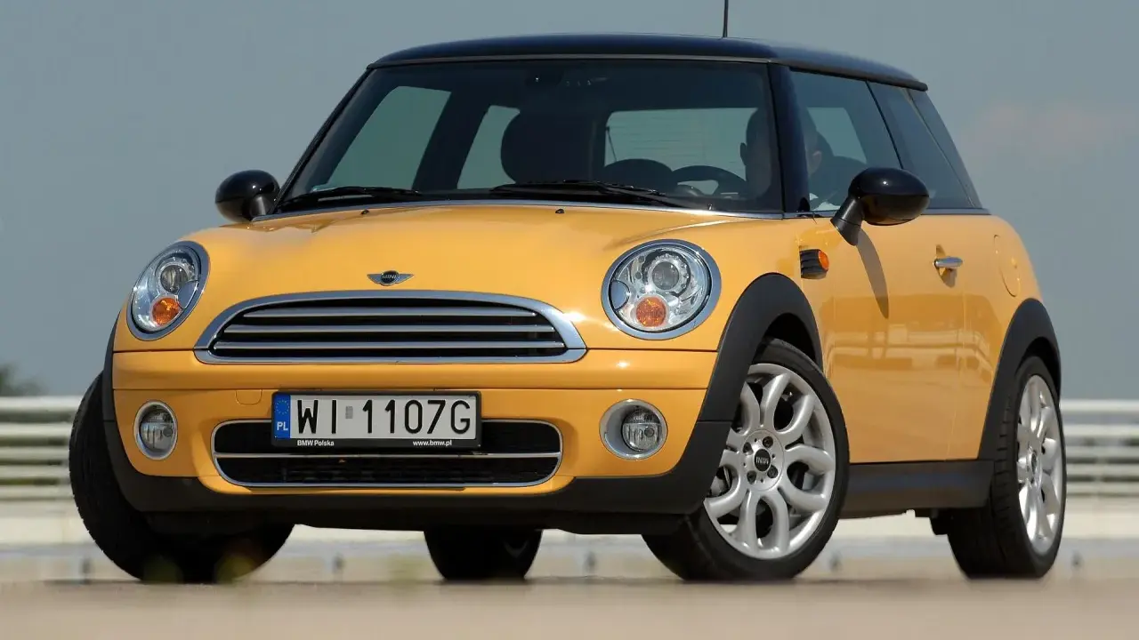 Żółty Mini Cooper, jedna z nowszych generacji, z czarnym dachem i felgami.