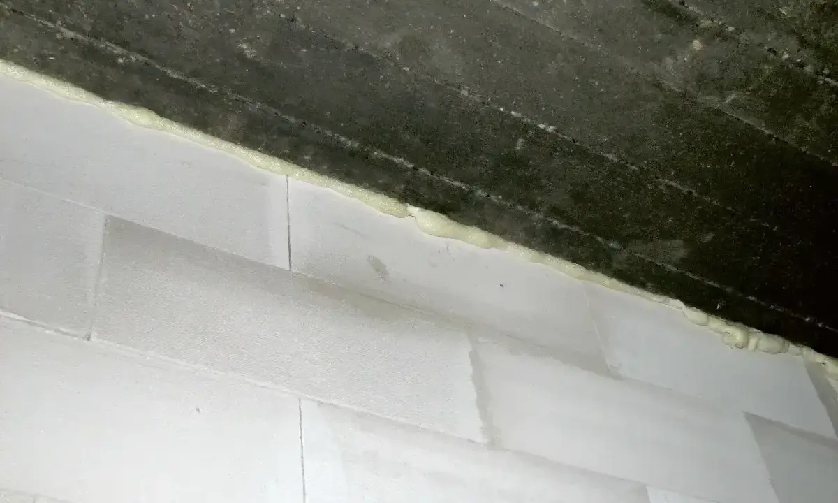 Piana montażowa, która jest rodzajem **elastomery**, uszczelnia połączenie między betonową belką a białymi bloczkami.