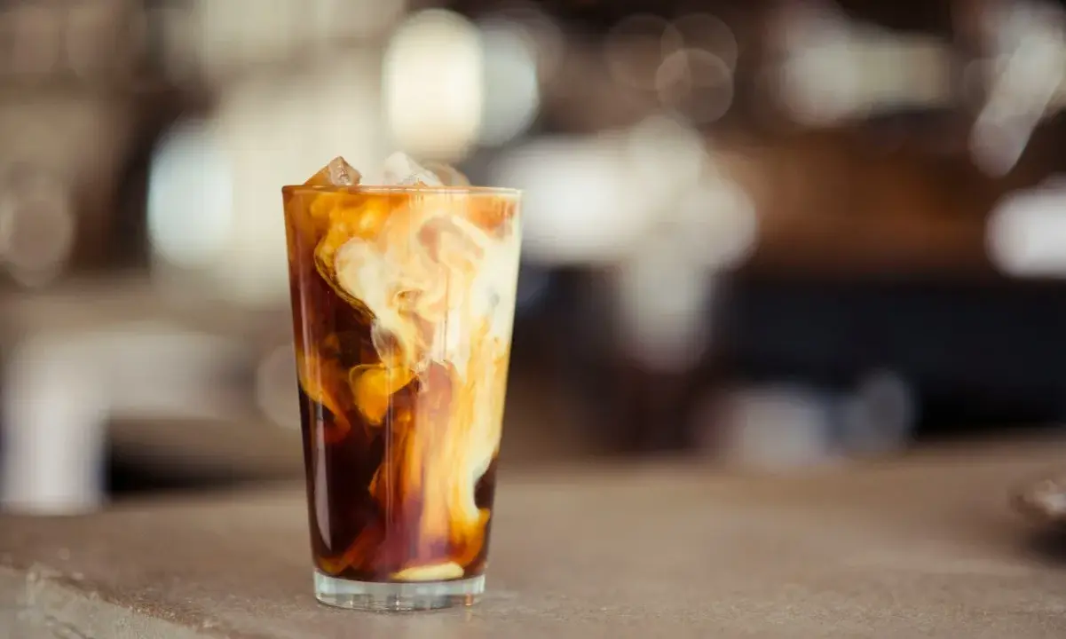 Ein Glas mit Eiswürfeln und cremiger Milch, die sich in dunklem Kaffee wirbelt. Perfekt für die Zubereitung von Cold Brew Coffee.