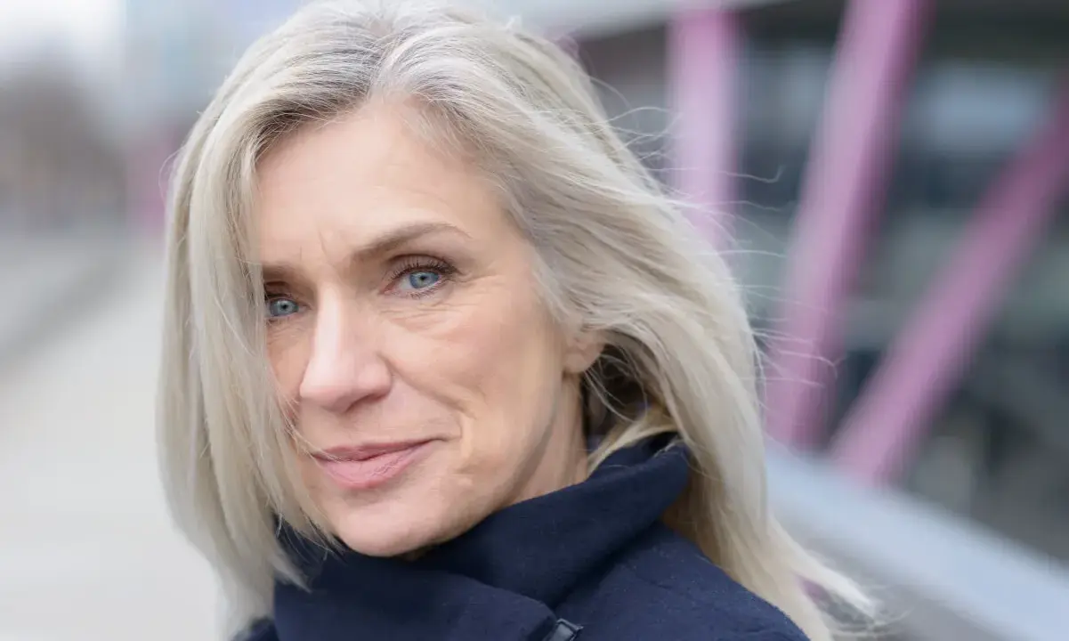 Donna con capelli bianchi e occhi azzurri, indossa un cappotto blu scuro. Un esempio di come vestirsi con i capelli bianchi.