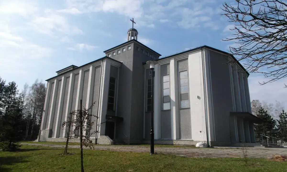 Nowoczesny kościół w Warszowicach, z charakterystycznymi pionowymi żłobieniami na fasadzie, pod błękitnym niebem.