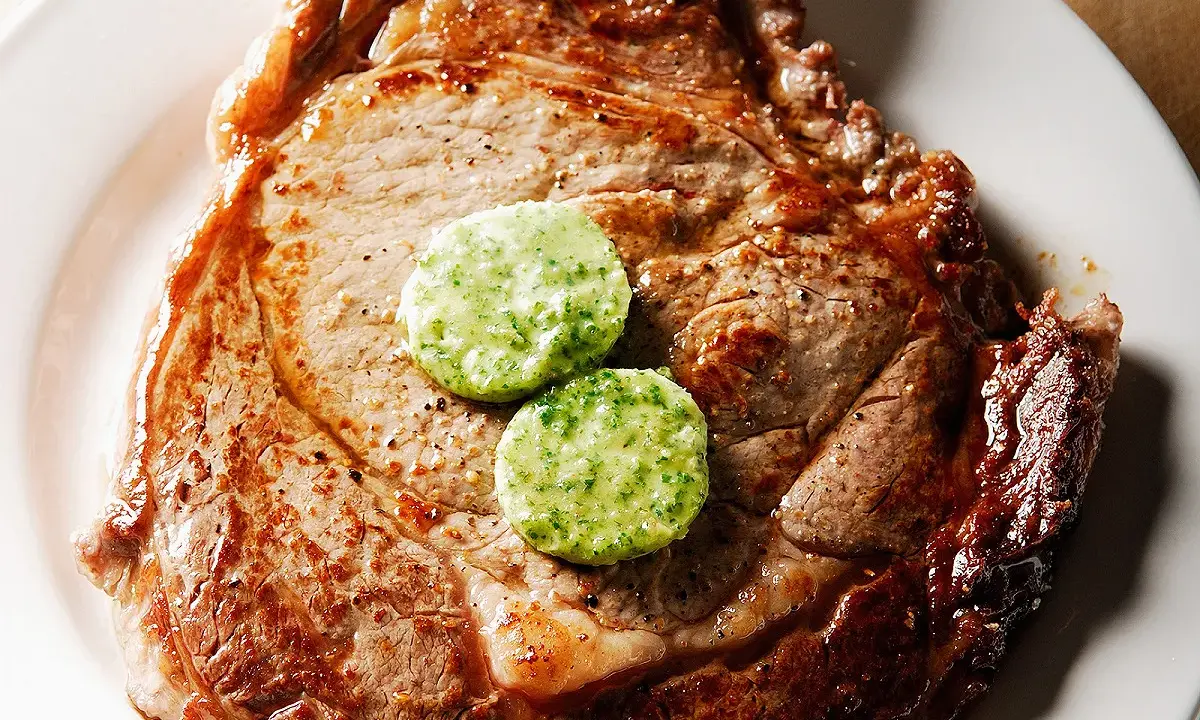 Un savoureux steak de bœuf, parfaitement grillé, est garni de deux rondelles de beurre maître d'hôtel, prêt à fondre.