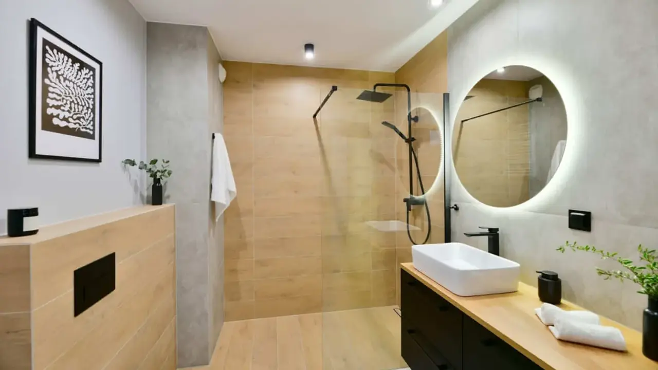 Baño moderno con ducha de suelo continuo, lavabo sobre encimera y espejo circular iluminado.