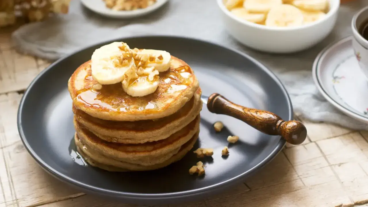 Pila de tortitas americanas con plátano y nueces, bañadas en sirope. Un desayuno perfecto.